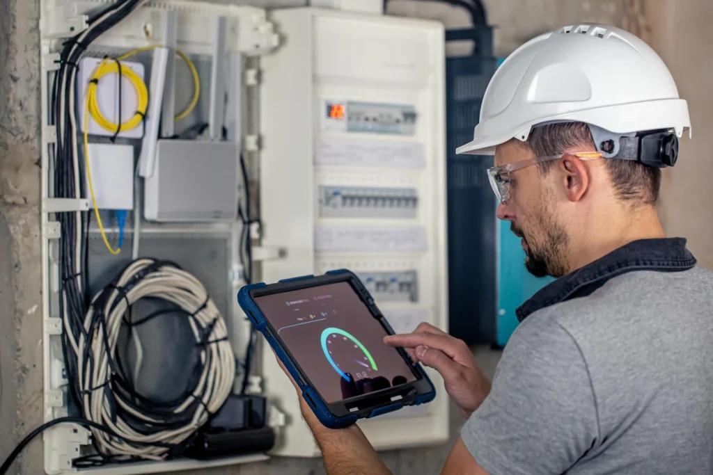 man electrical technician working switchboard with fuses uses tablet